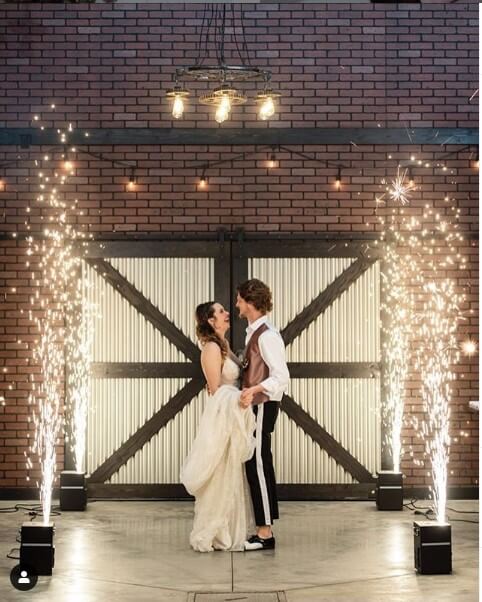 A couple is standing in front of a barn with fireworks.